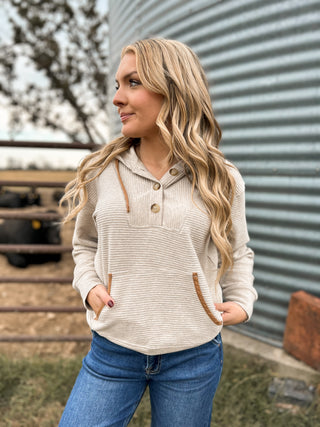Woman wearing a beige long-sleeve shirt with brown accents in front of a metal building.