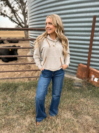 Woman wearing a beige hoodie and blue jeans standing in front of a metal silo on a farm.