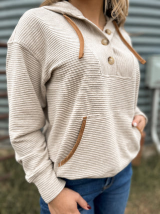 Beige ribbed sweater with brown accents worn by a person, blurred background