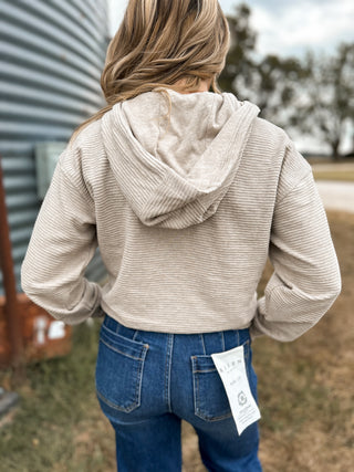 Person wearing a beige hoodie and blue jeans with a grain silo in the background
