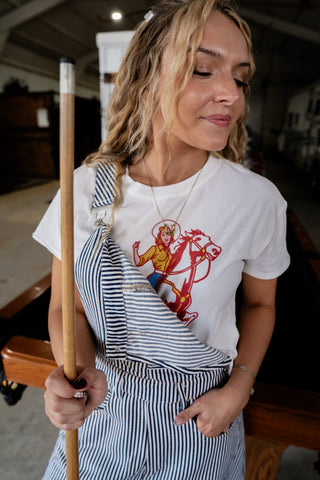 Woman holding a pool cue wearing a white t-shirt with a graphic design.