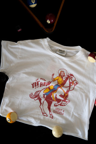White t-shirt with a graphic design of a cowgirl riding a horse, surrounded by pool balls on a black background.