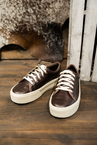 Brown sneakers with white soles on a wooden floor