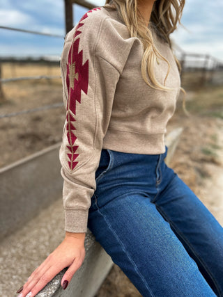 Person wearing a beige sweater with red geometric patterns and blue jeans, standing outdoors.