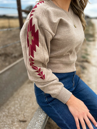 Person wearing a beige sweater with red geometric patterns sitting outdoors.