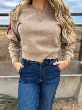 Person wearing a beige sweater and blue jeans with a blurred background
