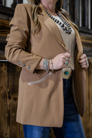 Person wearing a brown blazer with decorative buttons, standing against a wooden background.