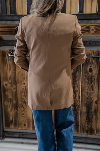 Person wearing a beige coat and blue pants standing in front of wooden doors.