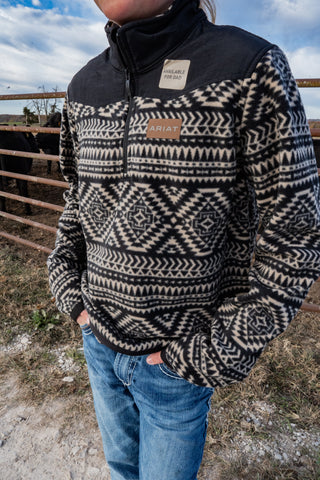 Person wearing a patterned fleece pullover with a visible brand logo, standing outdoors.