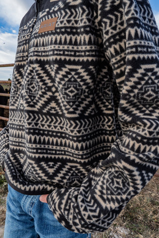 Person wearing a patterned jacket with a visible brand logo, standing outdoors.
