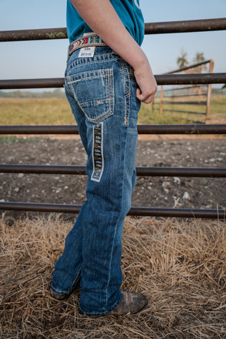 Person wearing blue jeans standing near a metal fence with a grassy field in the background.
