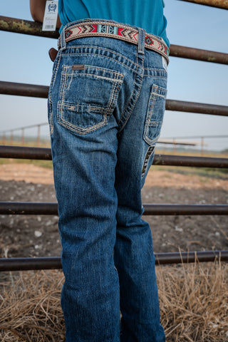 Person wearing blue jeans with a decorative belt standing behind a metal fence.