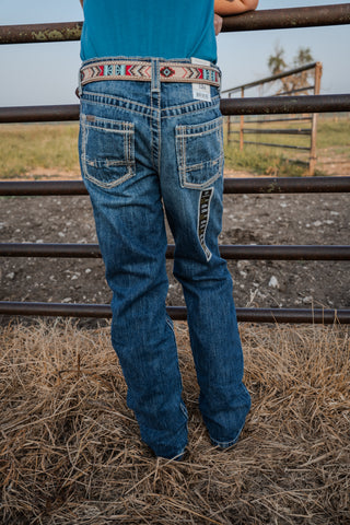 Person wearing blue jeans with a decorative belt standing in a fenced area.