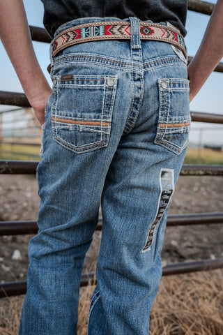 Person wearing blue jeans with a decorative belt, standing in an outdoor setting.