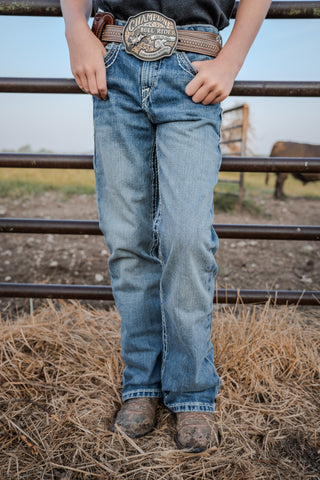 Person wearing blue jeans and a belt with a prominent buckle in an outdoor setting.