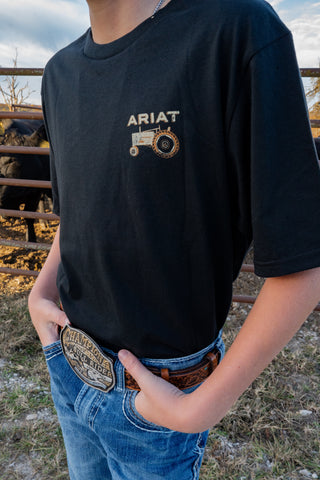 Person wearing a black Ariat t-shirt with a tractor logo outdoors.
