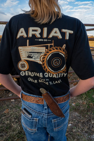 Person wearing an Ariat t-shirt with a tractor graphic outdoors.
