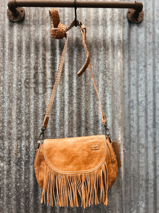 Brown leather handbag with fringe hanging on a metal wall.