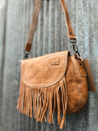Brown leather handbag with fringe details on a textured gray background