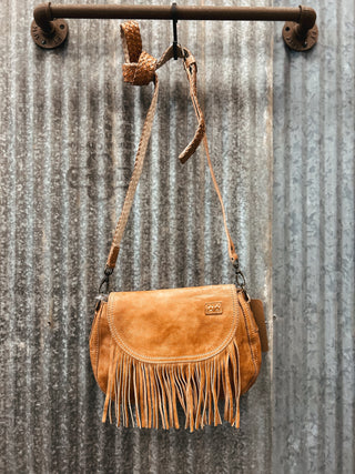 Brown leather handbag with fringe hanging on a metal wall.
