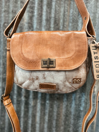 Brown leather crossbody bag with a textured strap against a corrugated metal background
