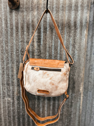 Vintage-style handbag with brown leather accents hanging on a textured metal wall.