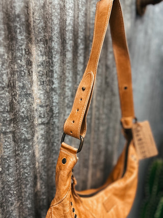 Brown leather handbag with strap against a textured wall