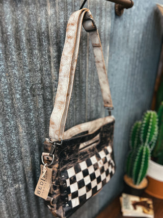 Handbag with checkered pattern and leather strap against a textured wall.