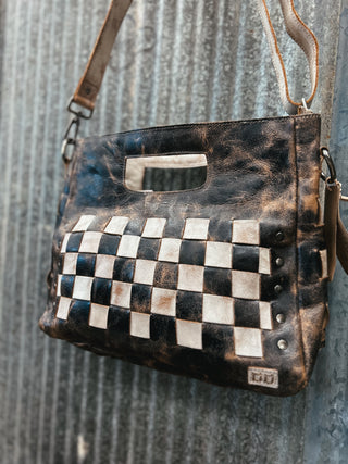 Vintage-style leather handbag with checkered pattern against a textured wall.