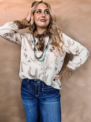 Woman wearing a patterned blouse and blue jeans against a beige background