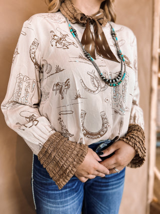 Person wearing a patterned blouse with cowboy graphics, holding a pair of scissors.