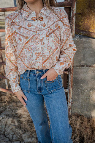 Person wearing a patterned blouse and blue jeans standing in front of a rustic background