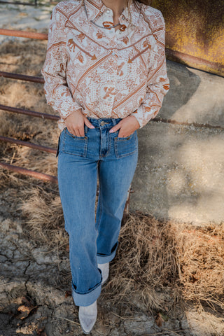 Person wearing a patterned blouse and blue jeans standing in front of a rustic metal gate.