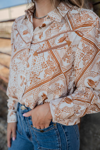 Person wearing a patterned blouse with long sleeves and blue jeans.