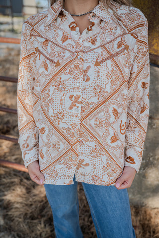 Person wearing a patterned shirt with long sleeves and blue jeans outdoors.