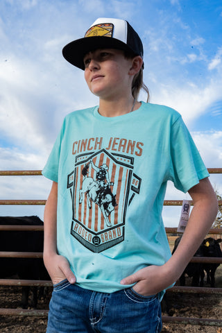 Person wearing a light blue t-shirt with a graphic design and text, standing outdoors with a cloudy sky.