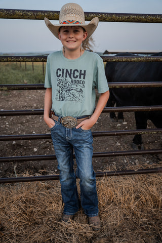 Young boy in a cowboy hat and Cinch Rodeo shirt standing in a barn.