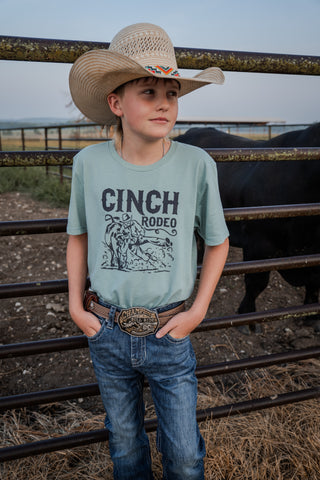 Child wearing a 'Cinch Rodeo' t-shirt with a cowboy hat and jeans, standing in front of a cow.