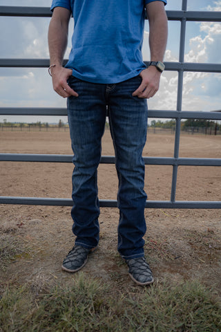 Person wearing a blue shirt and jeans standing in front of a metal gate with a cloudy sky.