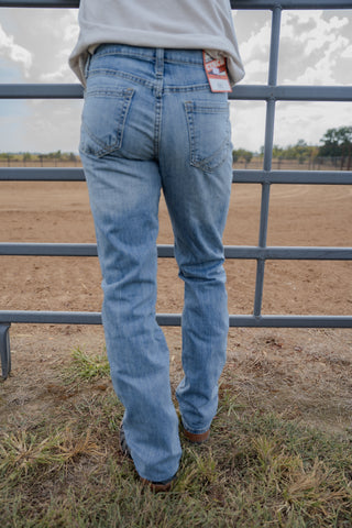 Person wearing blue jeans standing in a field with a metal fence in the background.