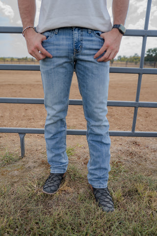 Person wearing light blue jeans standing in a field with a metal fence in the background.