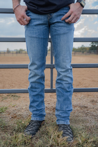 Person wearing blue jeans standing near a metal fence with a field in the background