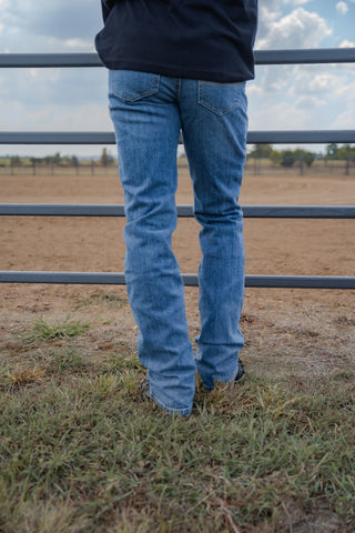 Person wearing blue jeans standing in a field with a fence in the background