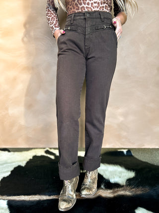 Person wearing brown pants with a leopard print top on a neutral background