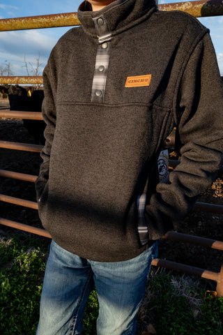 Person wearing a dark brown pullover with a brand logo, standing outdoors.
