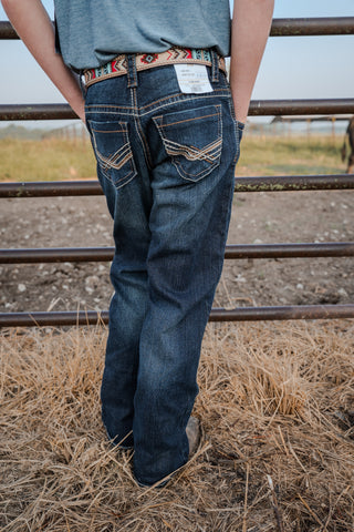 Person wearing blue jeans with a patterned belt standing in a field.