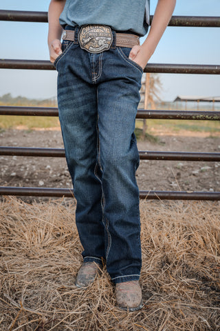 Person wearing blue jeans and a belt with a large buckle in an outdoor setting.