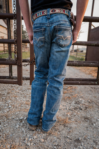 Person wearing blue jeans with a decorative belt standing behind a metal gate.