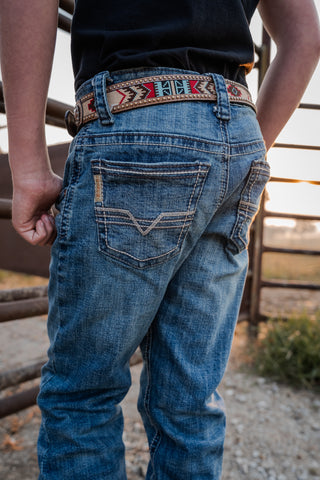 Person wearing blue jeans with a decorative belt, standing outdoors.