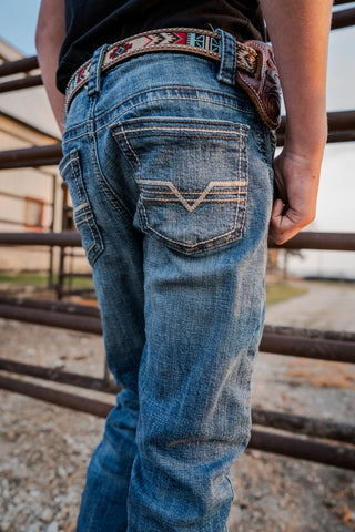 Person wearing blue jeans with a decorative belt, standing in front of metal bars.